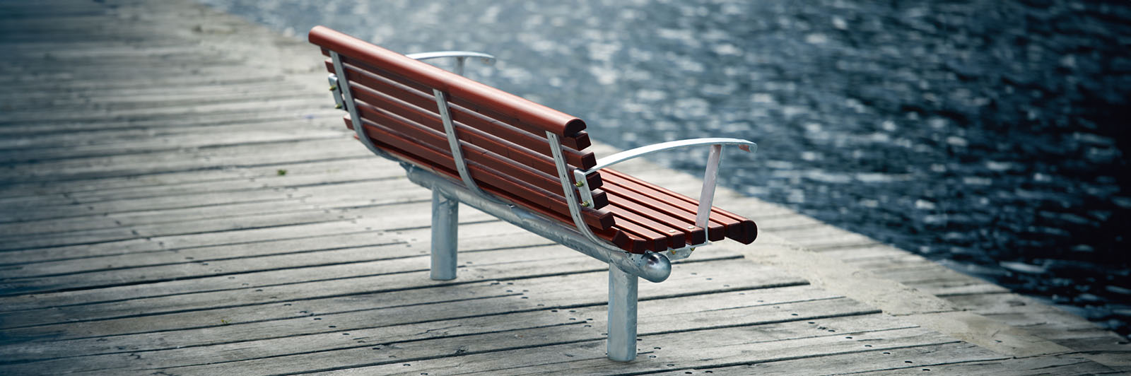 A park bench on a sidewalk next to a lake.